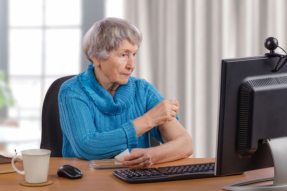 Ältere Frau sitzt vor einem Computer mit Webcam